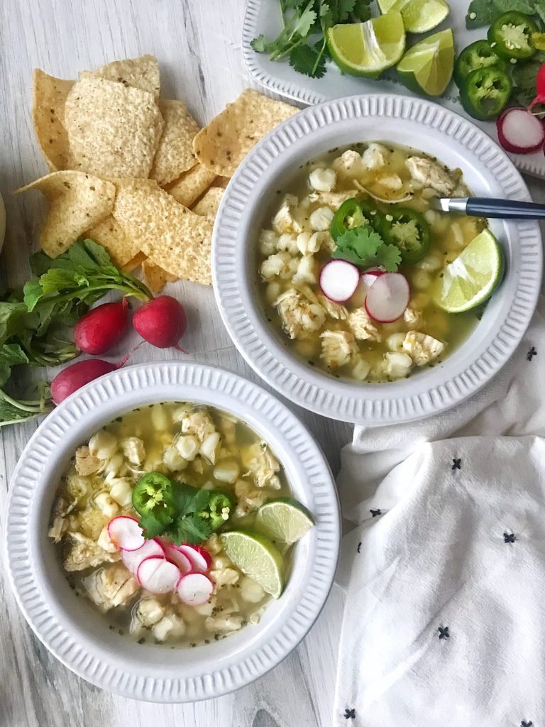 Two bowls of pozole verde with radishes to garnish. Tortilla chips on the side.