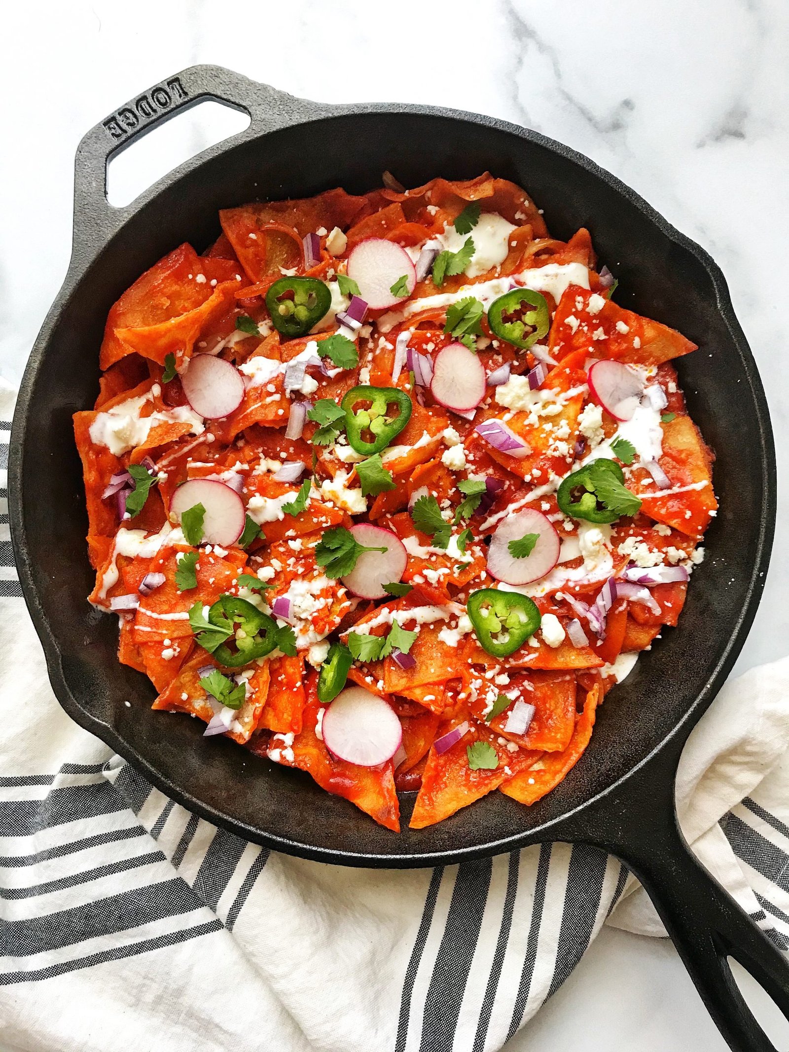 Chilaquiles Rojos (Red Chilaquiles) in cast iron skillet with cheese, sour cream, onions, jalapenos, radishes
