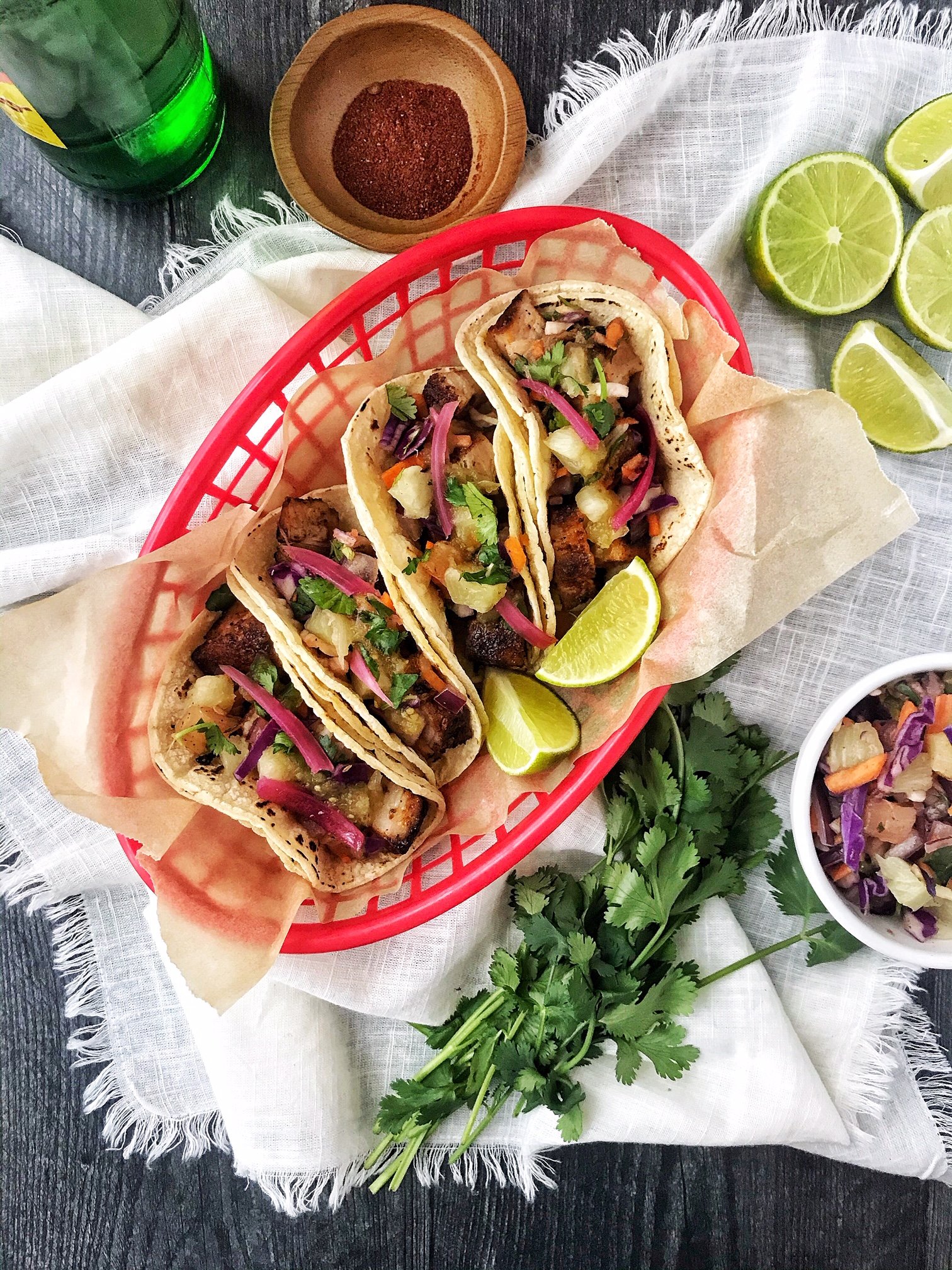 Pork belly tacos with pineapple slaw and red onion. Limes, chili powder, cilantro, and drink on the side.
