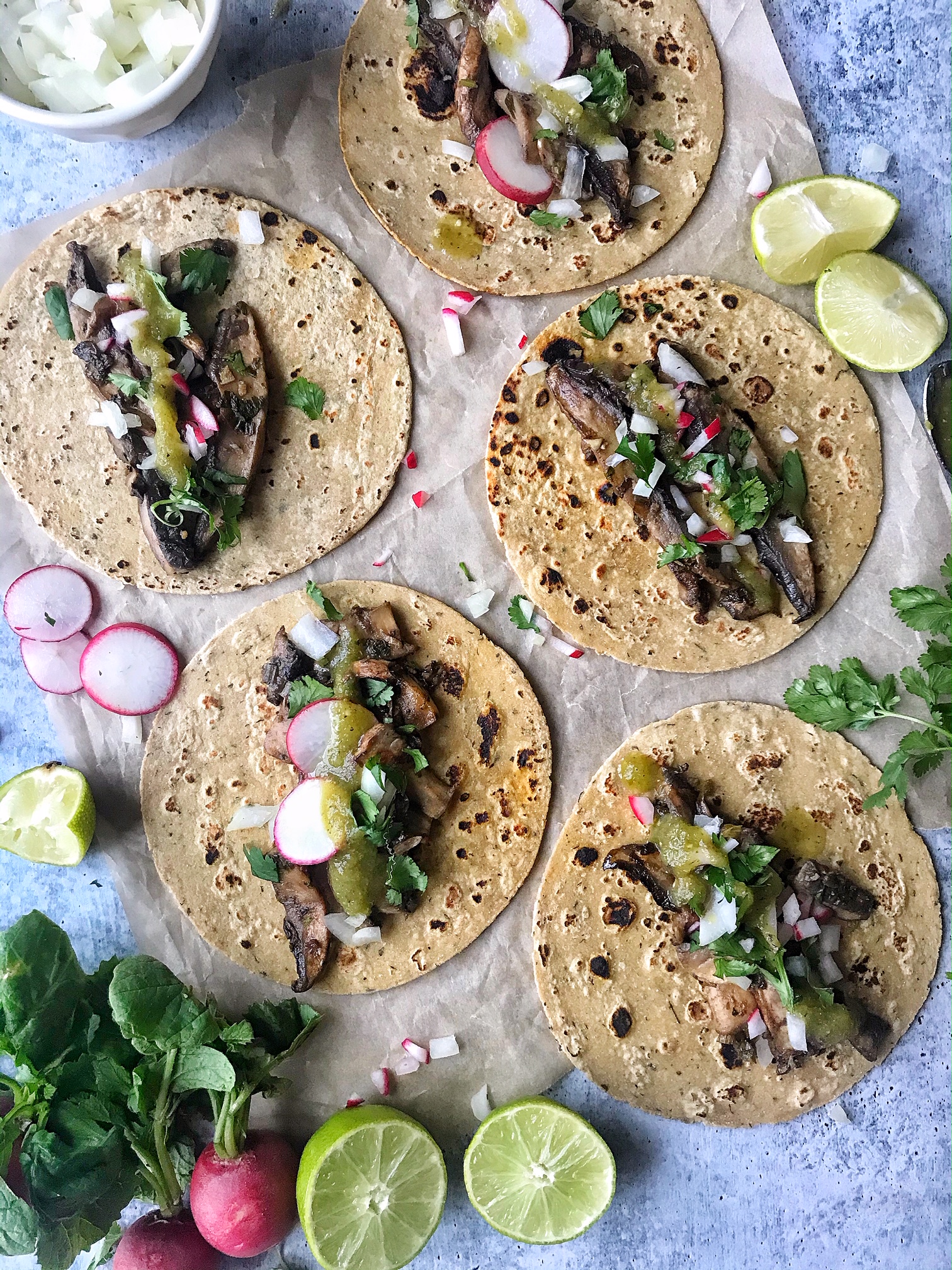 Mushroom Asada Tacos with onions, cilantro, salsa, and radishes. Laying flat on parchment paper.