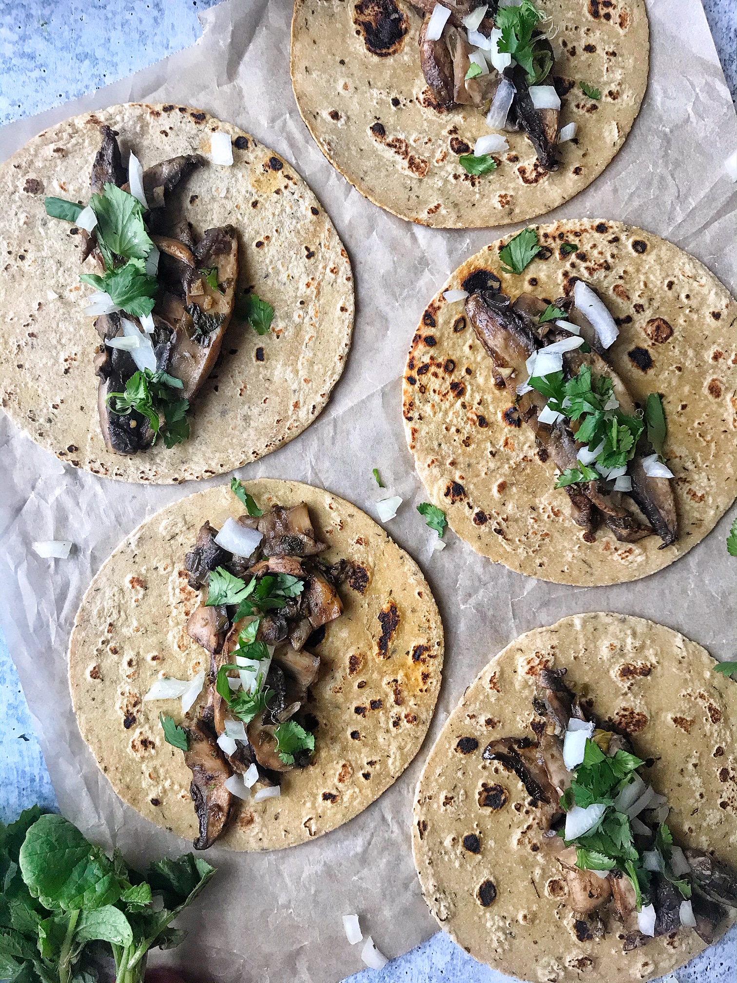 Mushroom Asada Tacos with onions and cilantro. Tacos laying flat on parchment paper.