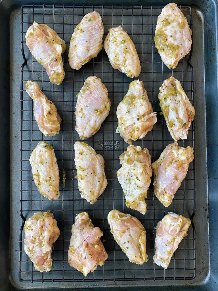 chicken wings coated with salsa verde on cooling rack on top of baking sheet.