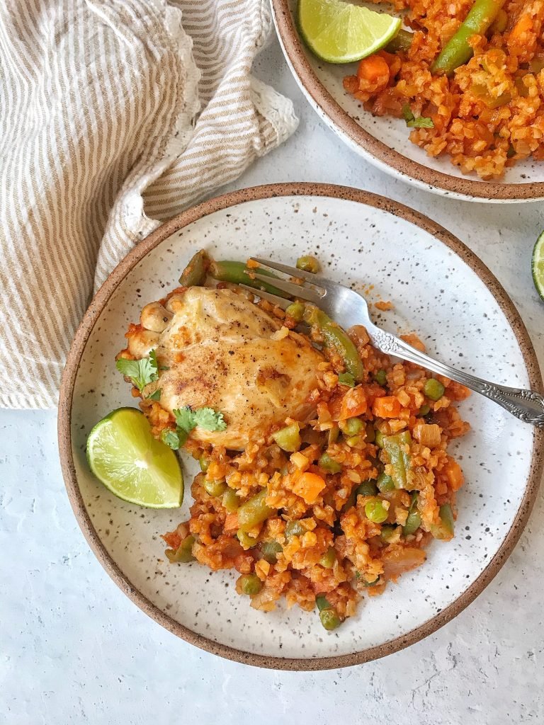 Chicken and cauliflower rice with vegetables on a white plate. Lime wedge on side.