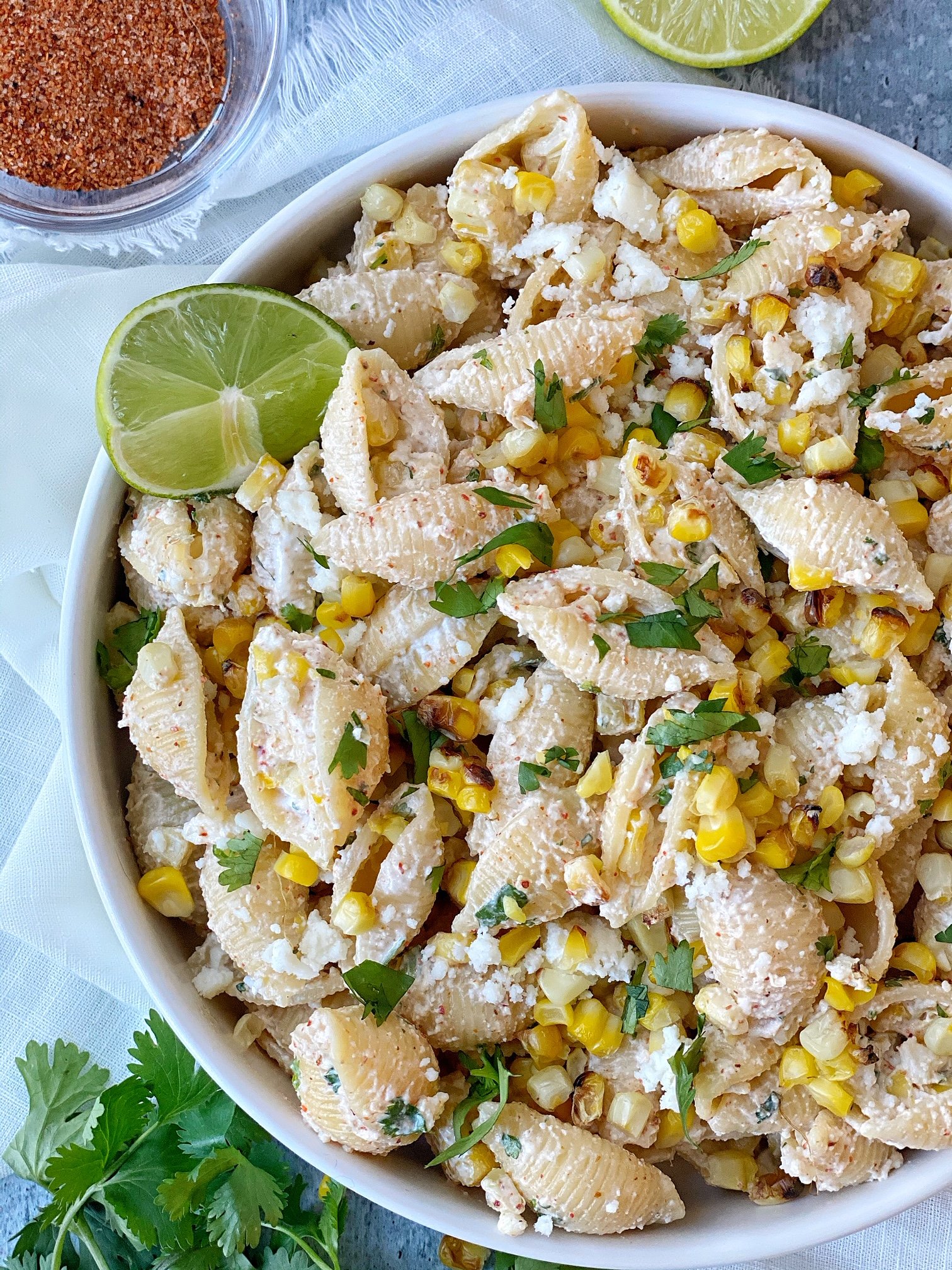 White plate with pasta salad with corn. Zoomed in image. Lime wedge garnish.