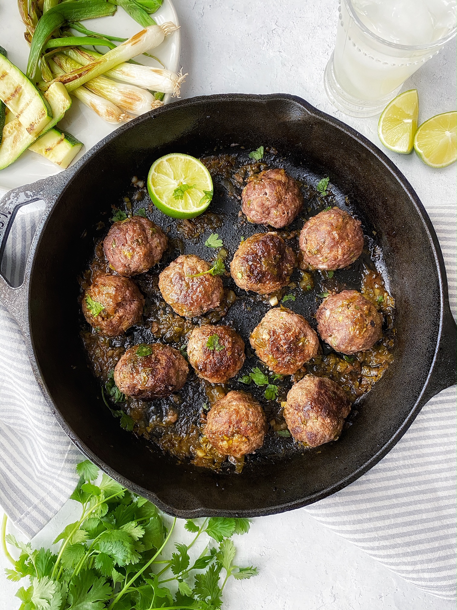 Cast iron pan with carne asada meatballs. Lime and cilantro garnish. Grilled zucchini and green onions on the side. 