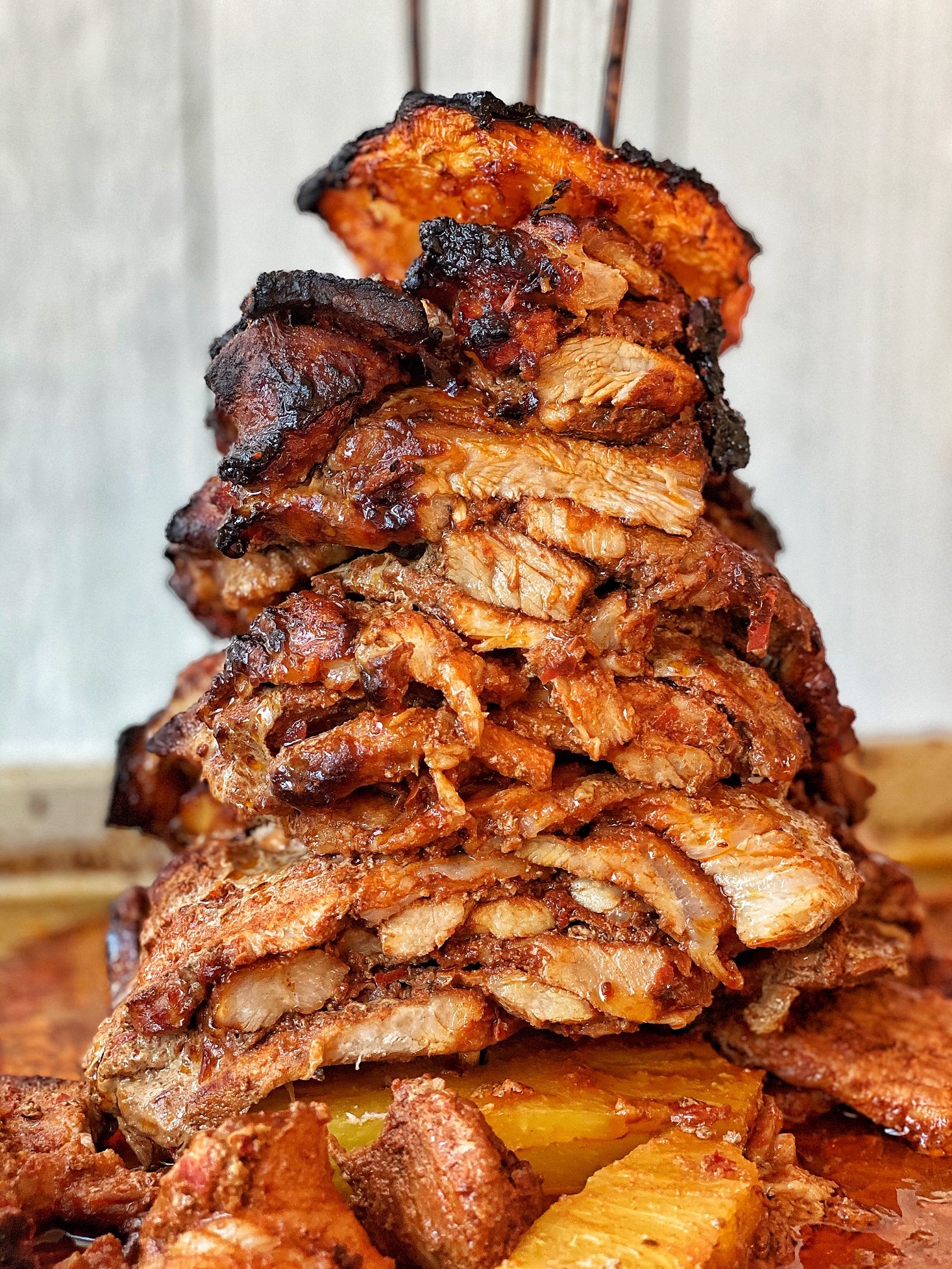 Carne Al pastor stacked on skewers with pineapple slices. Meat stack sliced.