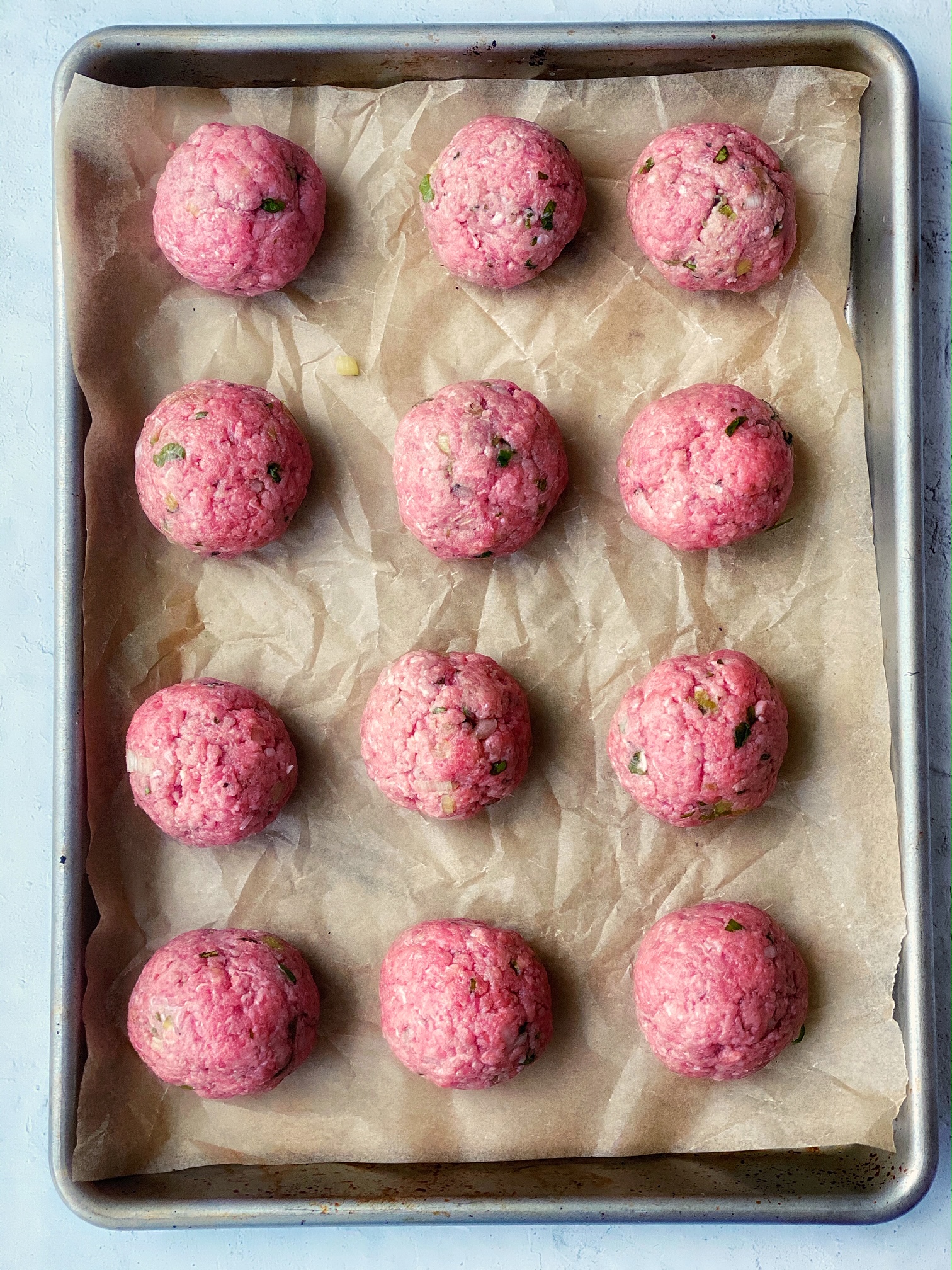 Sheet pan of rolled meatballs, uncooked.