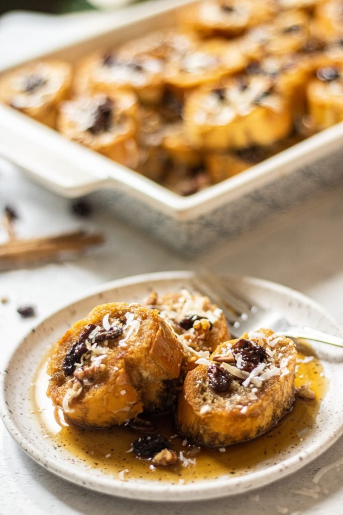 Capirotada, Mexican bread pudding, on a white plate. Topped with raisins, coconut flakes, and pecans.