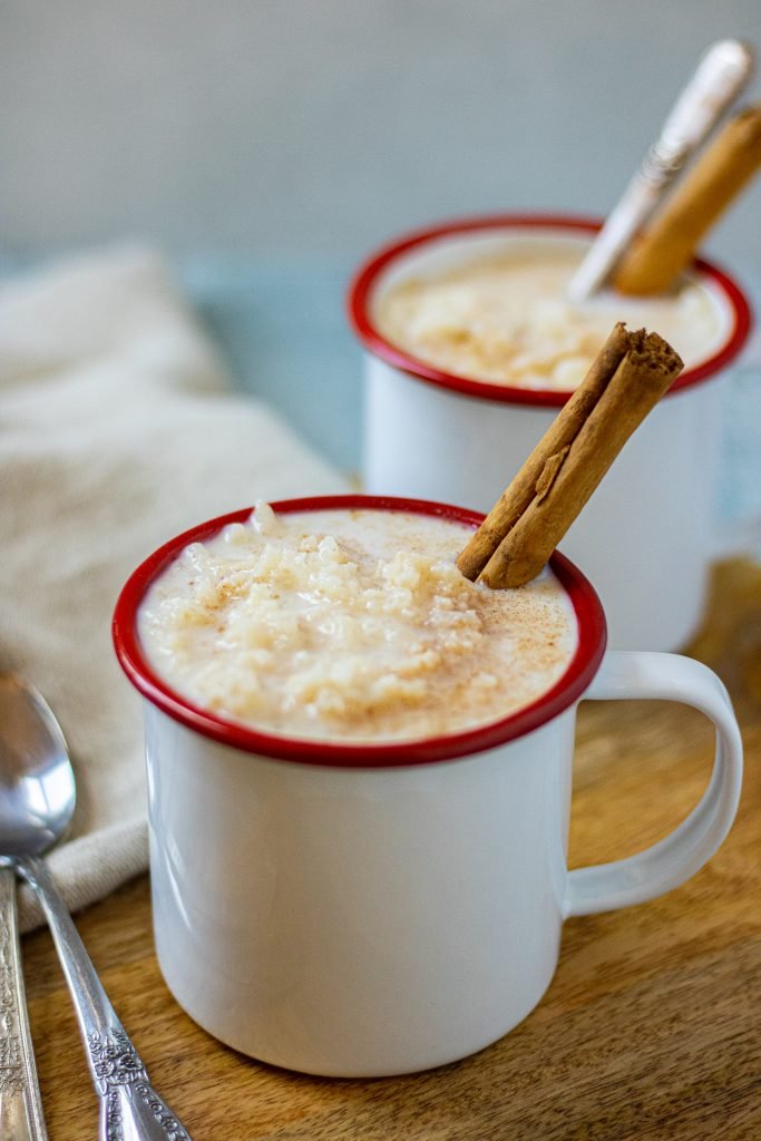 White mugs with red rims filled with arroz con leche. Garnished with a cinnamon stick.