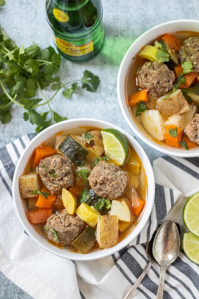 Tow white bowls full of albondiga soup with meatballs and vegetables.