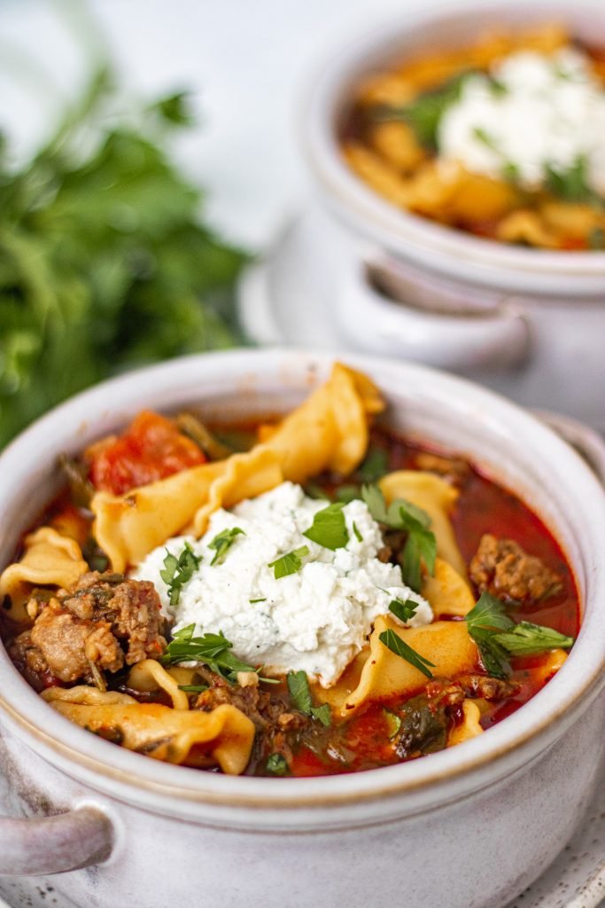 Close up of bowl with lasagna soup. Ricotta cheese on top. Parsley garnish.