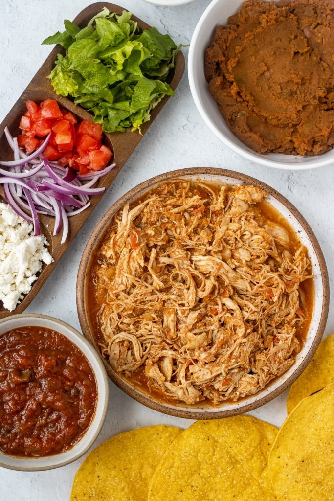 Ingredients for chicken tinga tostadas. Chicken tinga, salsa, cheese, onion, tomatoes, lettuce, refried beans, tostada shells