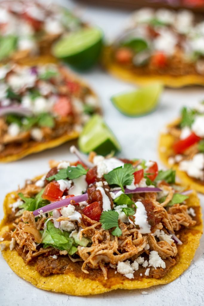 Close up of chicken tinga tostadas with tomato, onion, lettuce, sour cream, cheese.