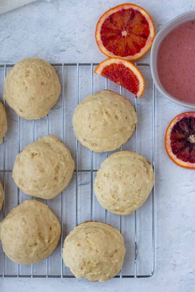 Blood orange ricotta cookies with no glaze. Bowl of glaze on side, slices of blood oranges
