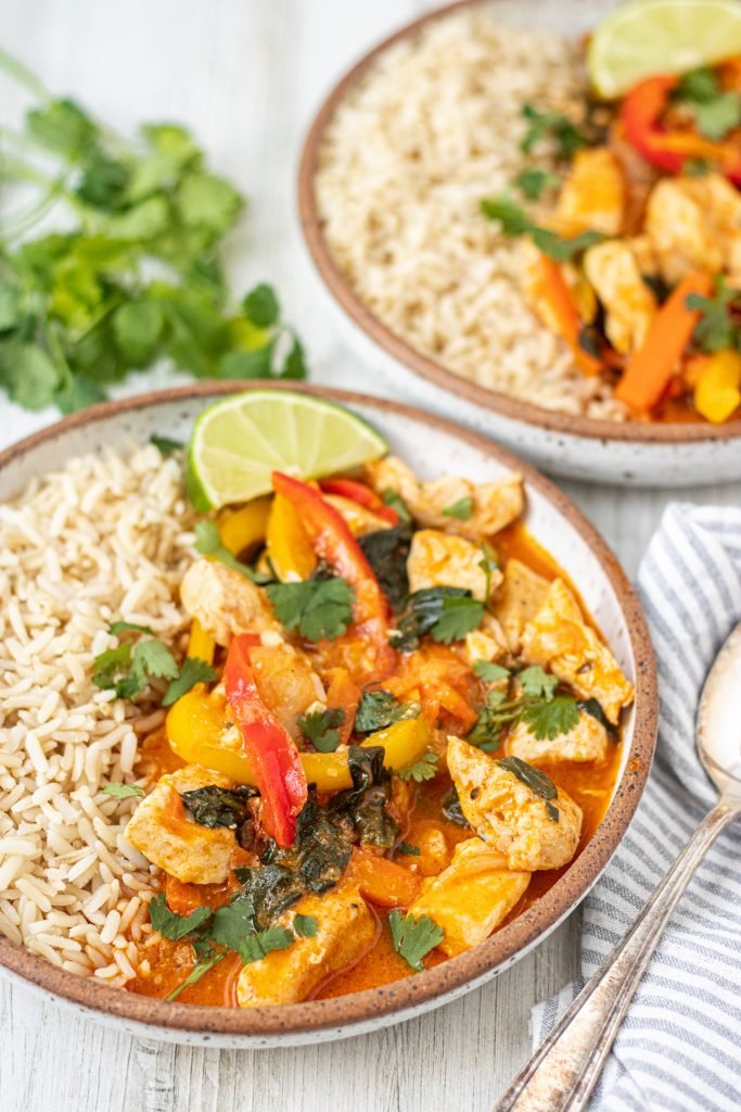 Two bowls of Thai Lemongrass Curry with peppers, brown rice on the side, lime and cilantro garnish.