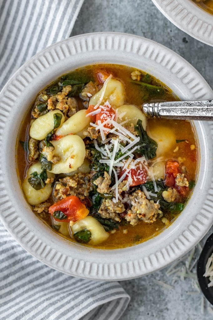 White bowl with gnocchi, spinach, sausage, and tomato soup. Parmesan garnish.