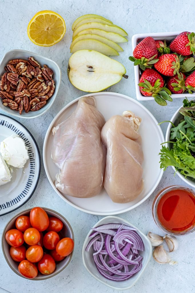 ingredients for grilled chicken salad with fried goat cheese. Chicken, greens, strawberries, pear, red onions, tomatoes, garlic, vinegar, pecans
